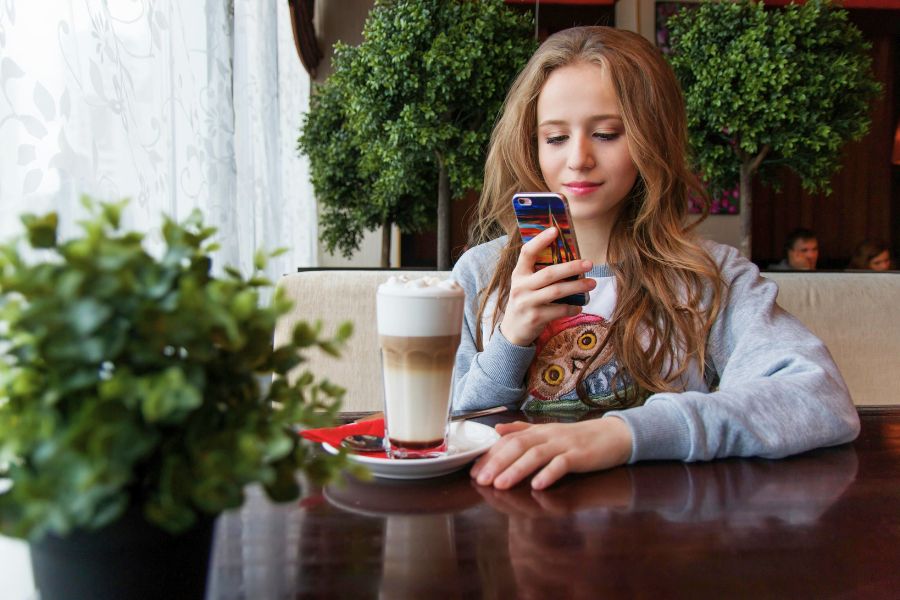 An image of a teen girl on a phone in a cafe, enjoying what she sees.